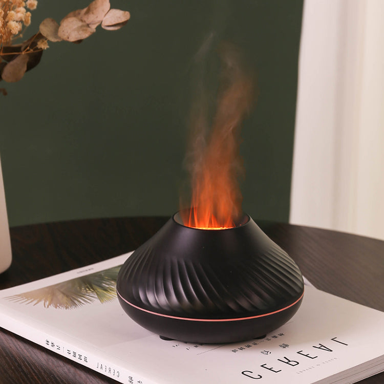 Black LavaLux Aromatherapy Diffuser on a book that is on a table, turned on, with the LED light set to orange, and mist coming out like a lit flame.