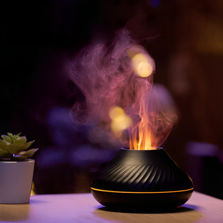 Black LavaLux Aromatherapy Diffuser on a table, turned on, with the LED light set to orange, and mist coming out like a lit flame. Next to it is a decorative plant. Dark-colored background.